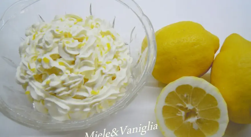 Una ciotola di panna montata con scorza di limone, accanto a limoni freschi. Perfetta per una ganache al limone leggera e profumata.
