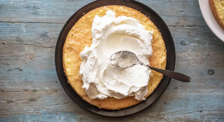 Una fetta di pan di spagna attende la sua deliziosa crema allo yogurt, spalmata con un cucchiaino.