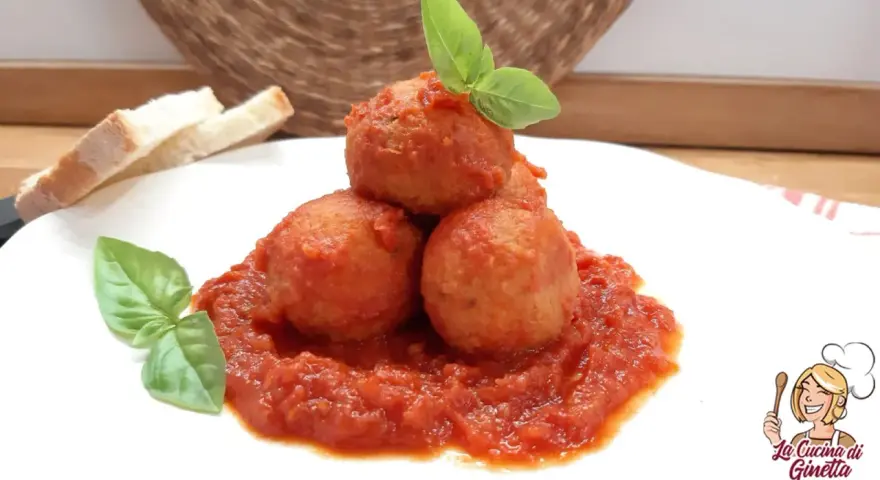 Polpette di pane in umido, un piatto confortante con pomodoro e basilico, accompagnato da fette di pane.