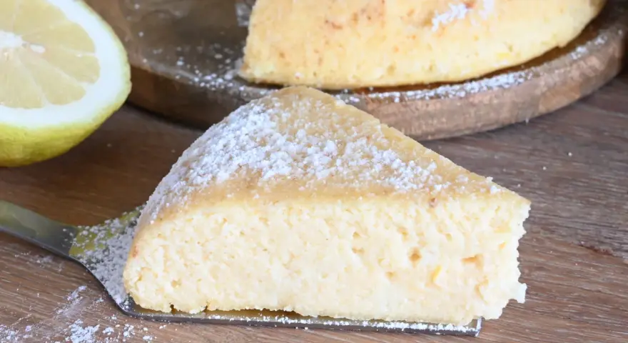 Una fetta di torta con semola, spolverata di zucchero a velo, accanto a un limone fresco.