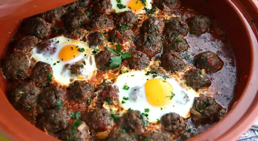 Polpette marocchine in umido con uova cotte nel tajine, guarnite con prezzemolo fresco.