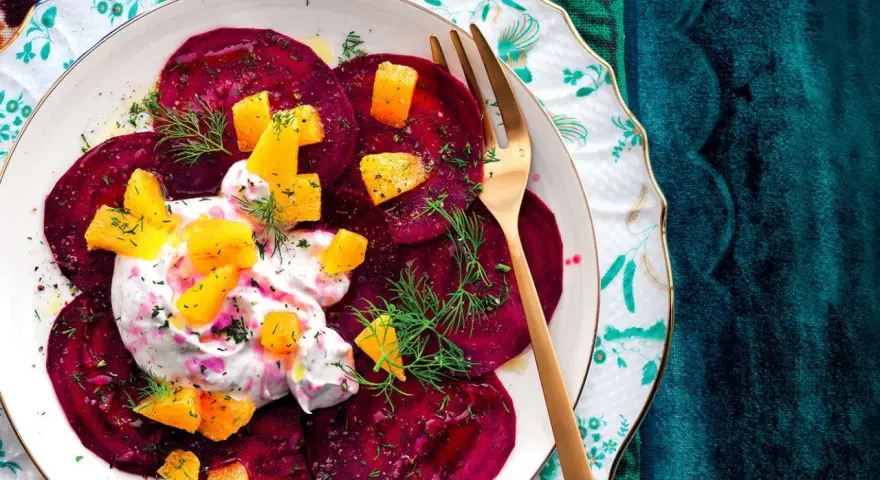 Delizioso carpaccio di barbabietola con crema, arancia e aneto su un piatto decorato.