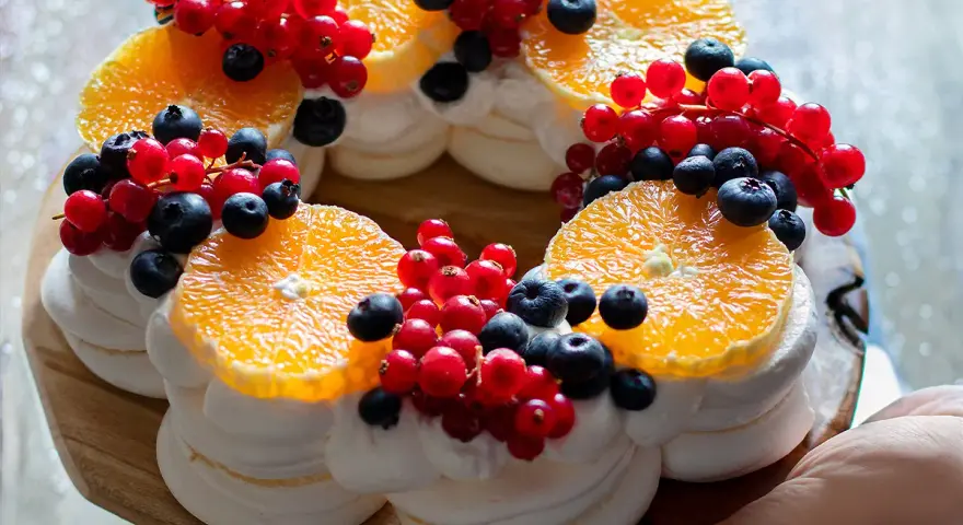 Delizioso tort pavlova a forma di corona, decorato con fette d'arancia, ribes rosso e mirtilli.