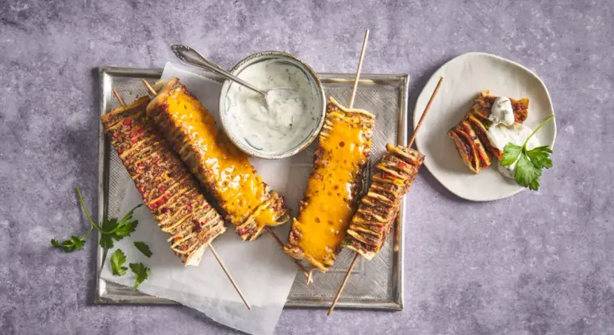 Tortilla kebab su spiedini, alcuni ricoperti di formaggio fuso, serviti con salsa allo yogurt e prezzemolo.