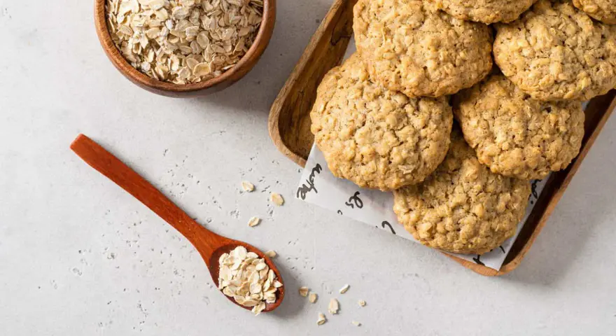 Biscotti di avena dorati e croccanti, con fiocchi d'avena in una ciotola e un cucchiaio.