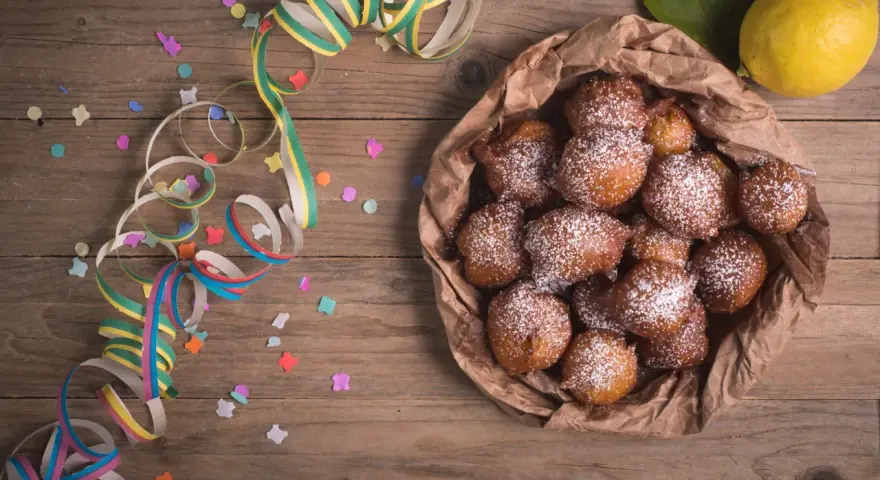 Castagnole abruzzesi cosparse di zucchero a velo, pronte per Carnevale, con coriandoli e stelle filanti su tavola di legno.