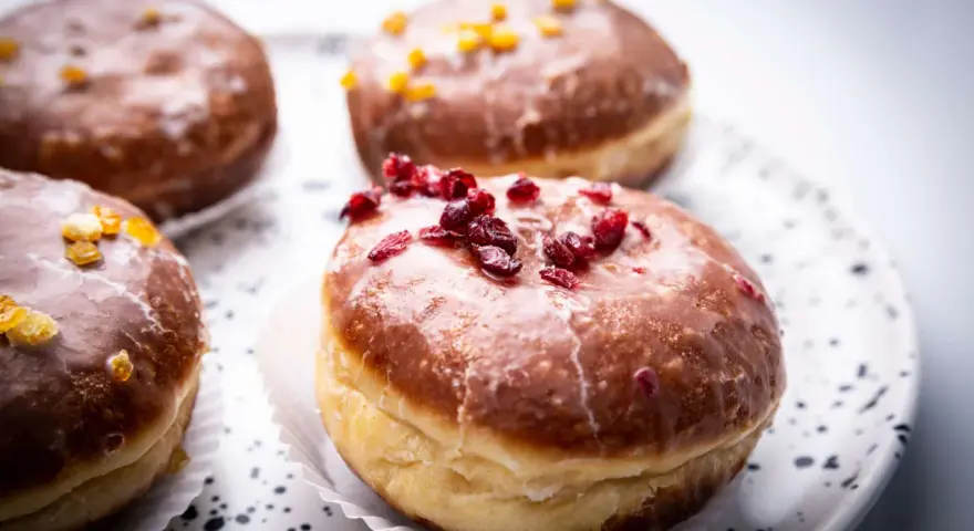 Paczki ricchi e golosi, con glassa lucida e decorazioni di frutta secca. Un invito a provare il paczki przepis perfetto.