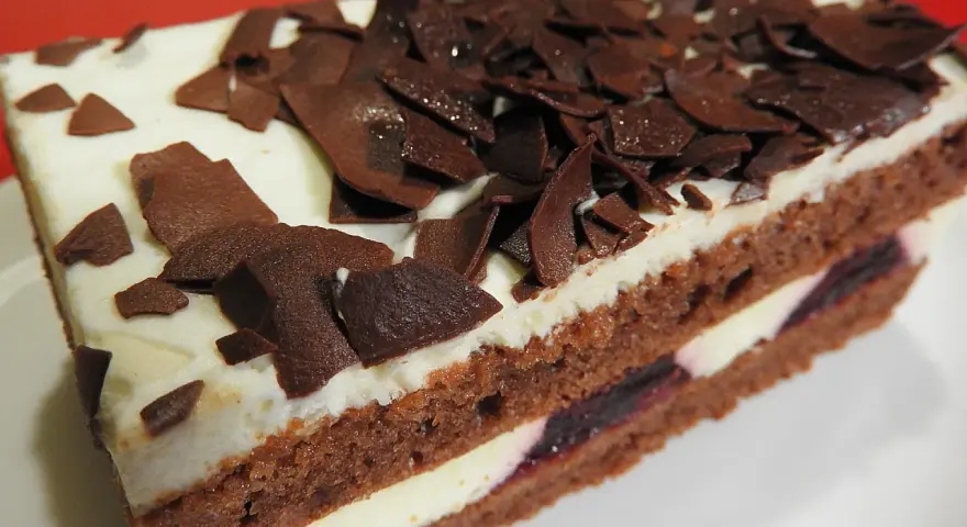 Una fetta di torta foresta nera di Montersino, con pan di Spagna al cacao, panna montata e ciliegie, decorata con riccioli di cioccolato.