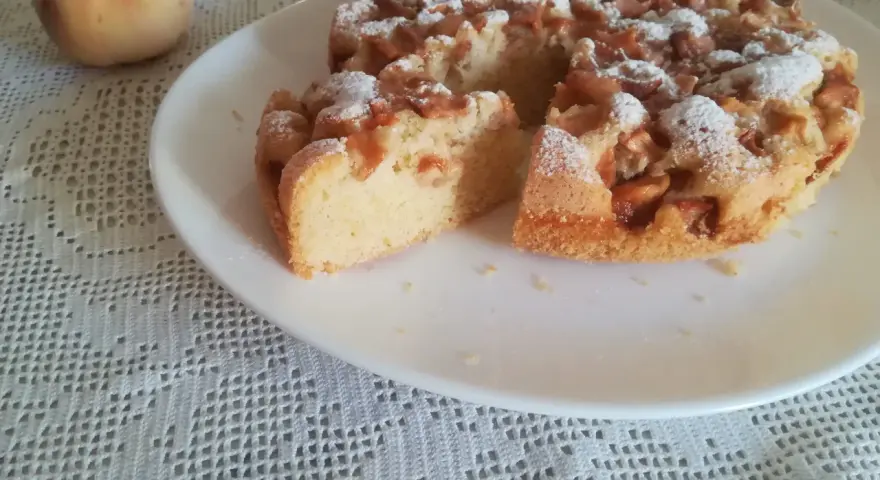Delizioso ciasto z brzoskwiniami, cosparso di zucchero a velo, su un piatto bianco, accanto a una pesca fresca.