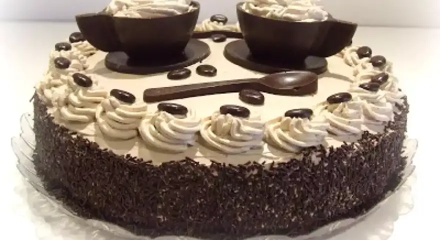 Torta decorata con ciuffi di crema al caffè, chicchi di cioccolato e due tazzine di cioccolato riempite di crema. Un vero capolavoro per gli amanti del bagna al caffè.