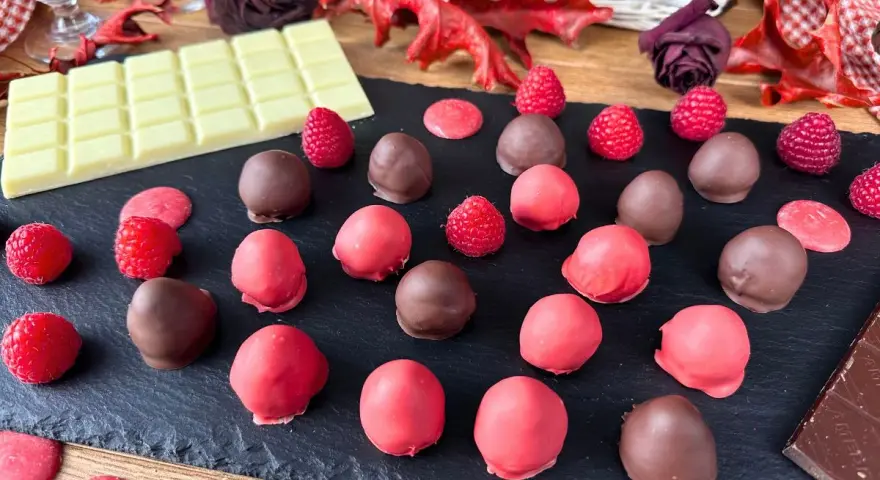 Cioccolatini al lampone, alcuni ricoperti di cioccolato fondente, altri di rosa, con lamponi freschi e tavoletta di cioccolato bianco.