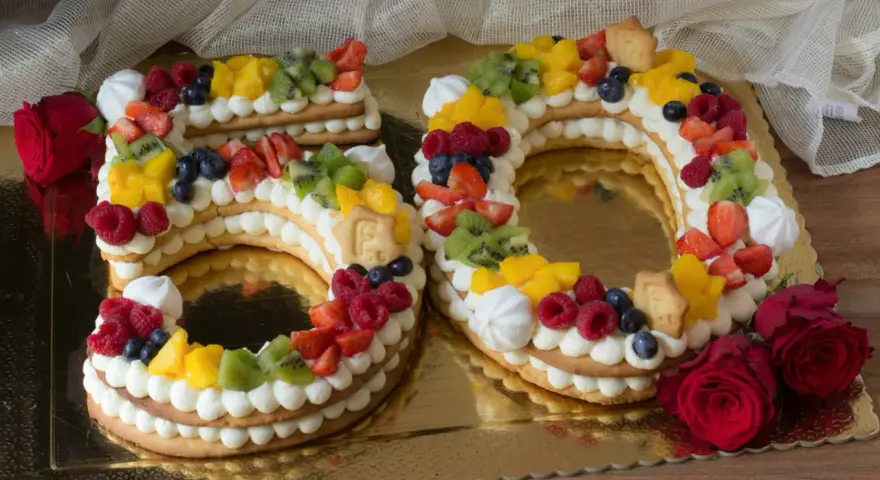 Torta 50 anni con panna, frutta fresca e biscotti a forma di numero. Un dolce colorato e delizioso per festeggiare un traguardo importante.