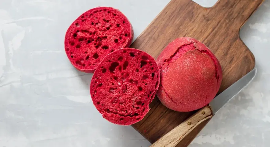 Pane alla barbabietola, un panino rosso vibrante tagliato a metà su un tagliere di legno, pronto per essere gustato.