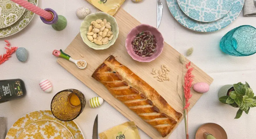 Torta pasqualina senza uova dorata, con mandorle e pinoli, decorata con uova colorate e candela pasquale.
