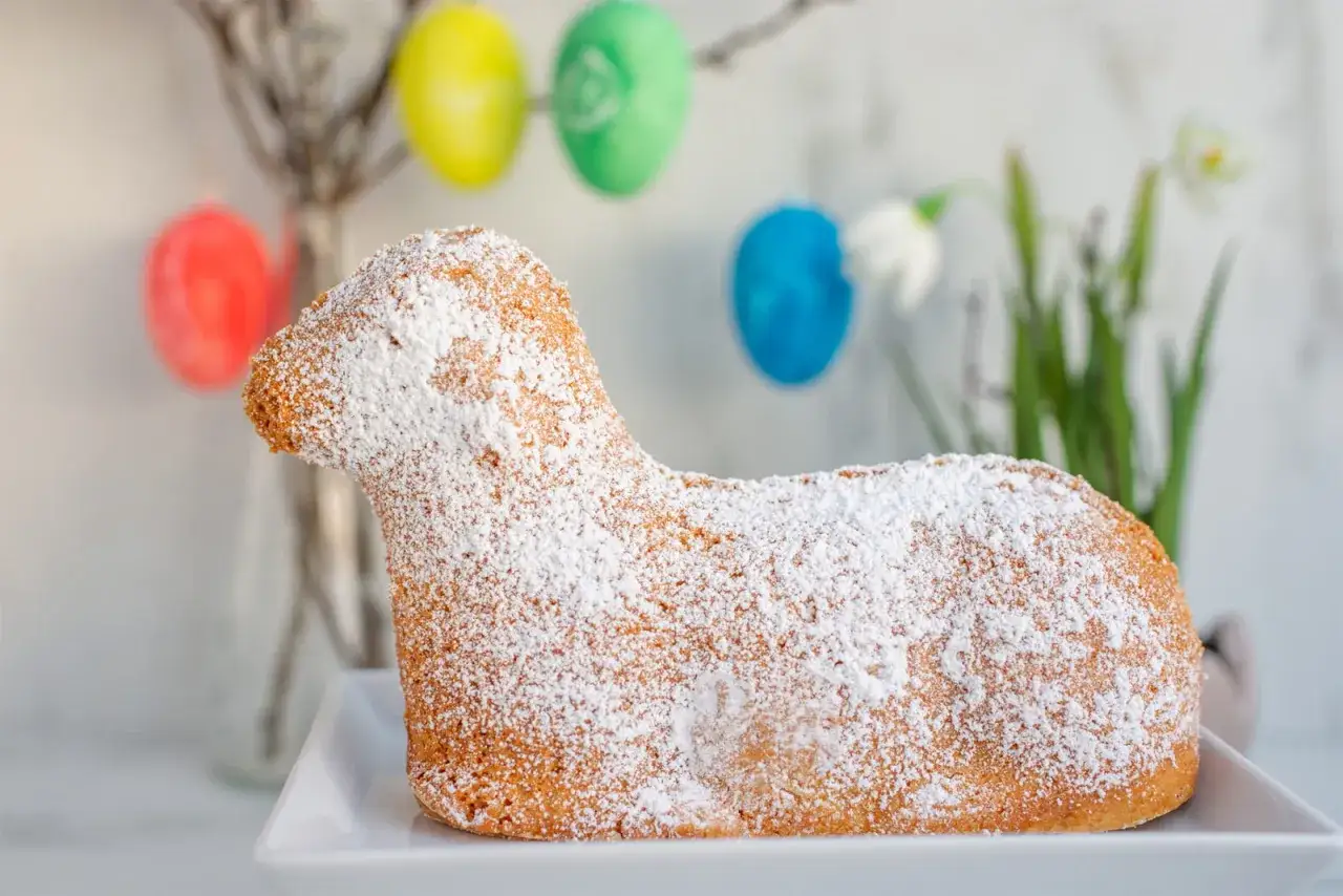 Dolce a forma di agnello pasquale, il baranek wielkanocny, cosparso di zucchero a velo. Uova colorate sullo sfondo.
