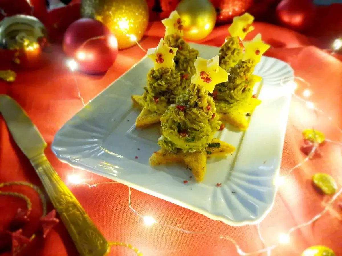 Alberelli di patate decorati con stelle gialle, su un piatto bianco, circondati da luci natalizie e palline dorate e rosse.