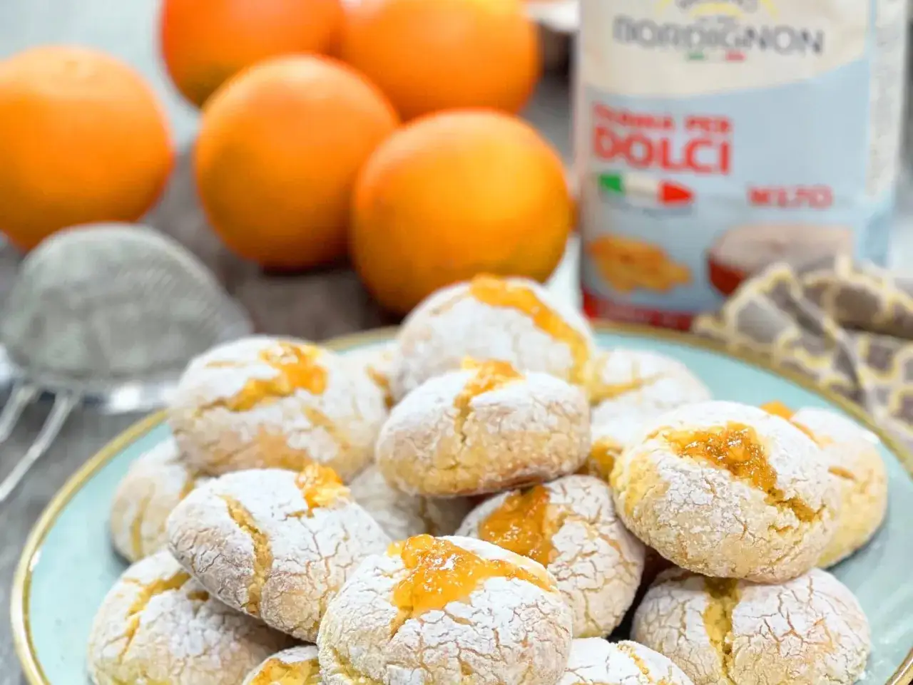 Biscotti all'arancia ricetta della nonna, cosparsi di zucchero a velo e ripieni di marmellata. Sullo sfondo, arance fresche e farina per dolci.