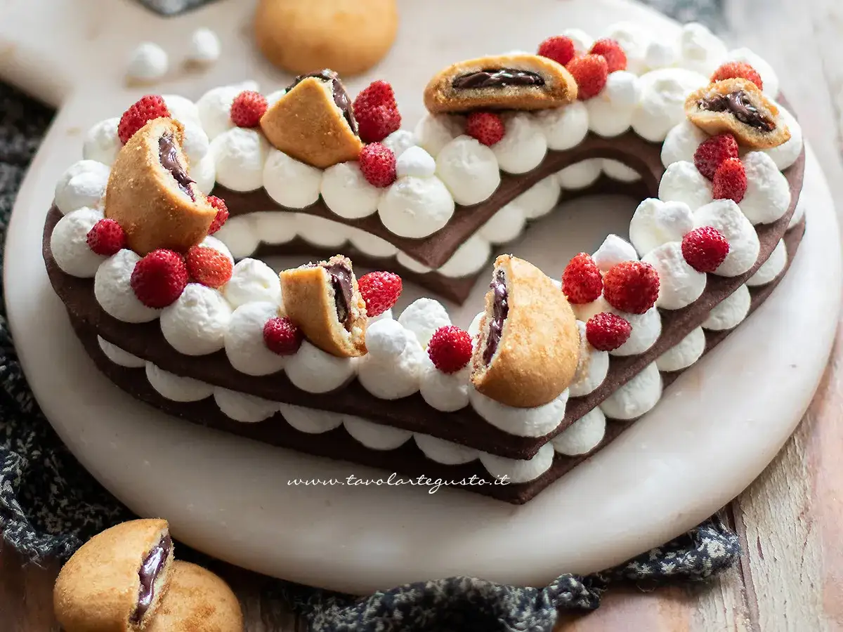 Cuore di pasta biscotto al cacao per cream tart, decorato con panna, fragoline e biscotti ripieni.