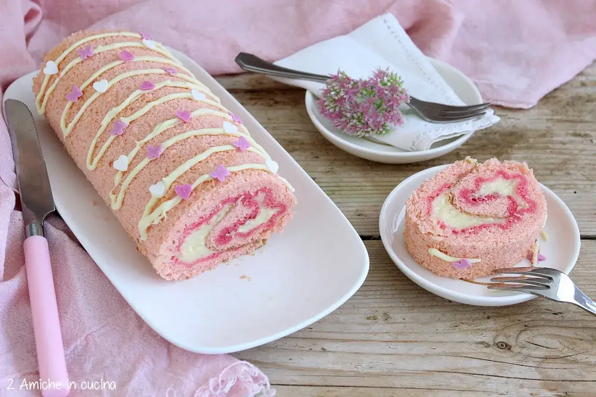 Rotolo rosa decorato con glassa bianca e cuoricini, che ricorda le pesche dolci abruzzesi. Una fetta &egrave; gi&agrave; servita su un piattino.