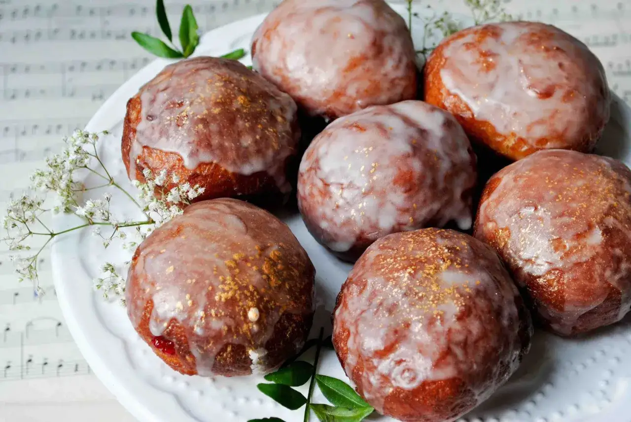 Paczki ricoperti di glassa bianca e decorati con polvere dorata, pronti per essere gustati seguendo un ottimo paczki przepis.
