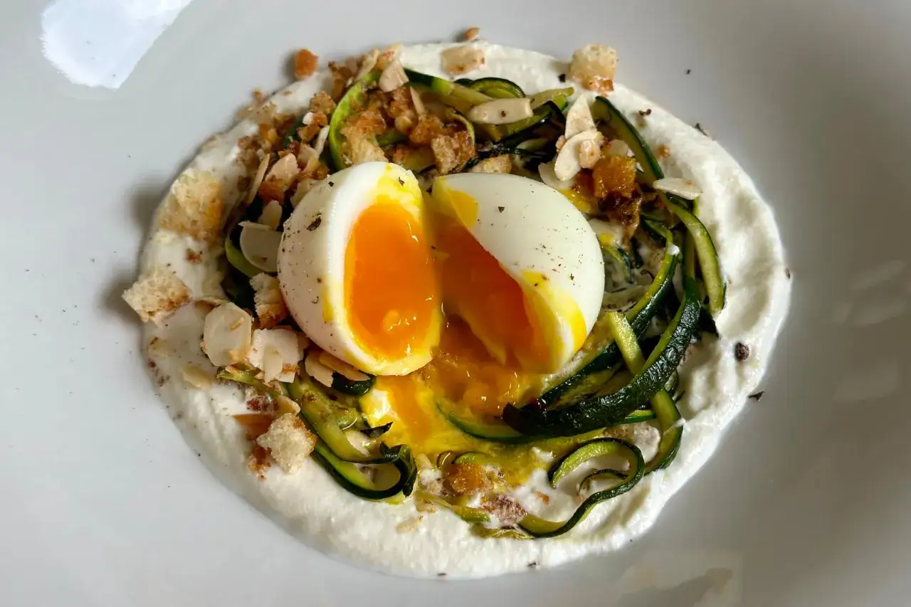 Uovo barzotto su crema di formaggio, zucchine a julienne, mandorle e crostini. Il tuorlo colante promette un sapore delizioso.