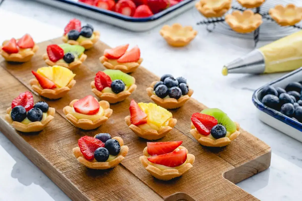 Deliziosi cestini di frutta ricetta, pronti per essere gustati. Fragole, mirtilli, kiwi e ananas decorano queste crostatine.