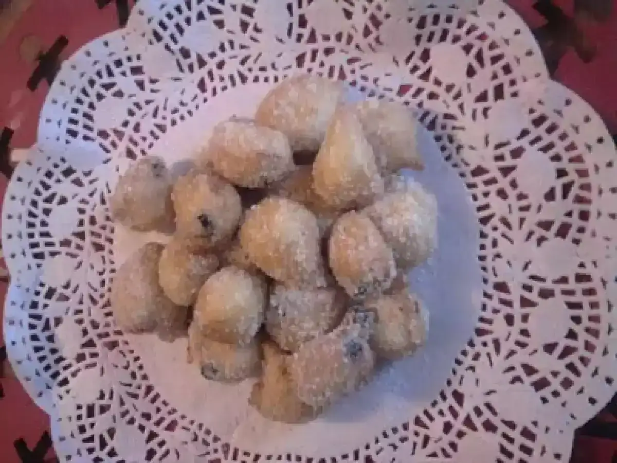 Un mucchietto di castagnole montersino, dolcetti dorati e zuccherati, adagiati su un centrino di carta pizzo.