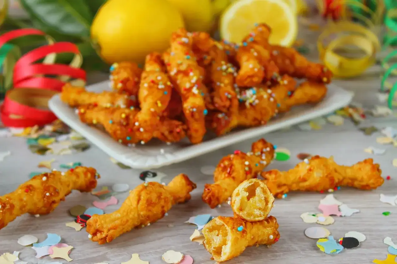 Dolci fritti a forma di fiocco, guarniti con zuccherini colorati e limoni sullo sfondo. Perfetti per celebrare con gusto!