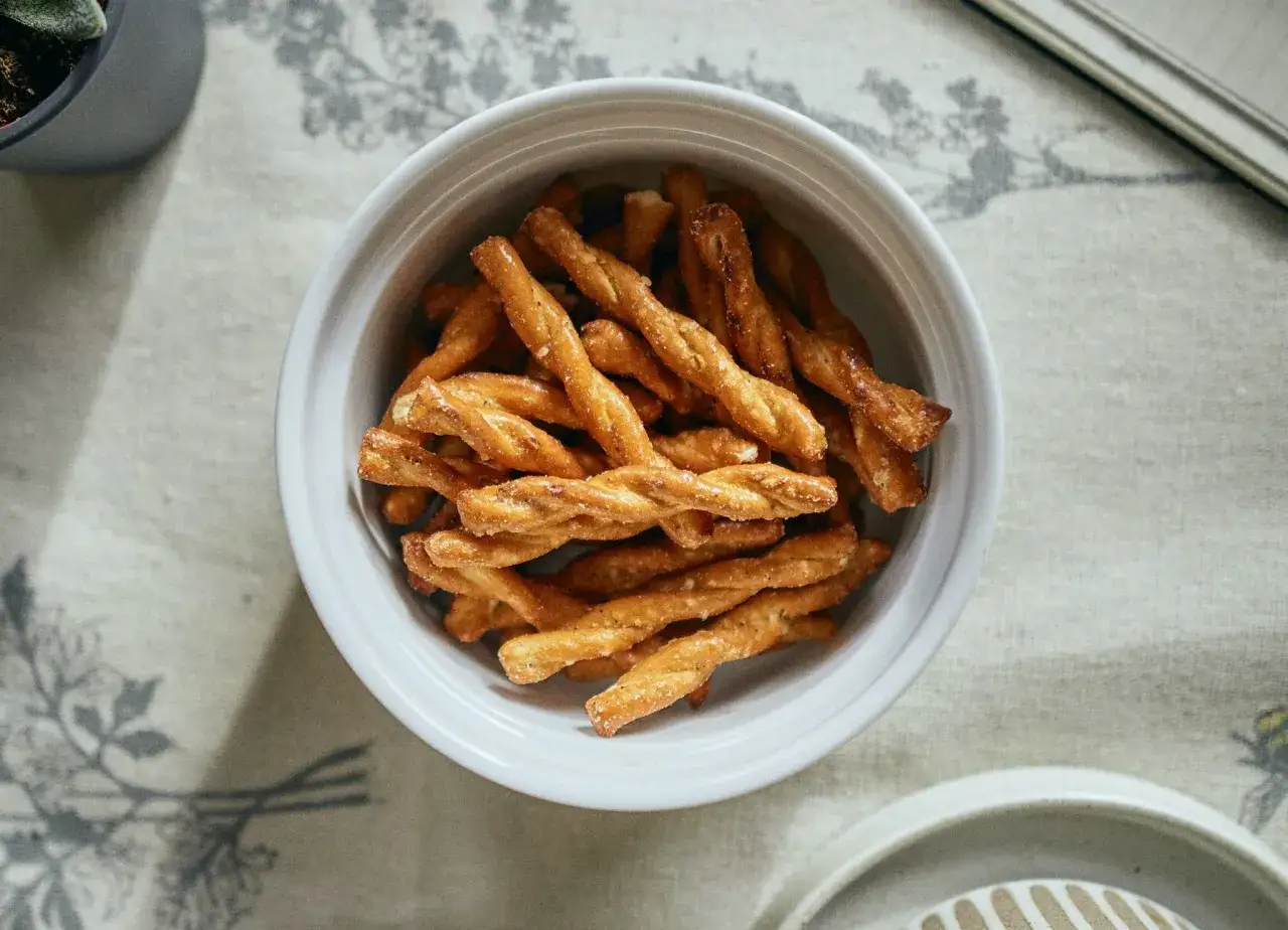 Una ciotola bianca piena di croccanti pizza sticks intrecciati, perfetti per uno spuntino.