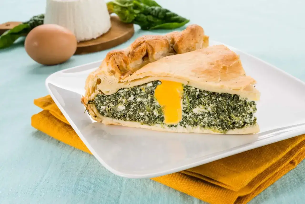 Una fetta di crostata pasqualina salata con ripieno di spinaci e ricotta, con un uovo intero al centro.