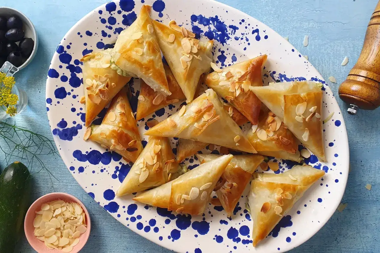 Triangolini di pasta fillo con mandorle, cotti al forno, su un piatto bianco con schizzi blu.