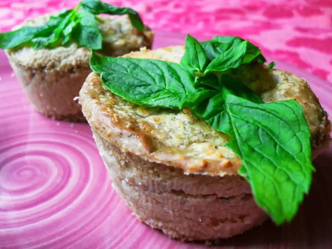 Sformato di melanzane leggero, dorato e profumato, guarnito con foglie di basilico fresco su un piatto rosa.