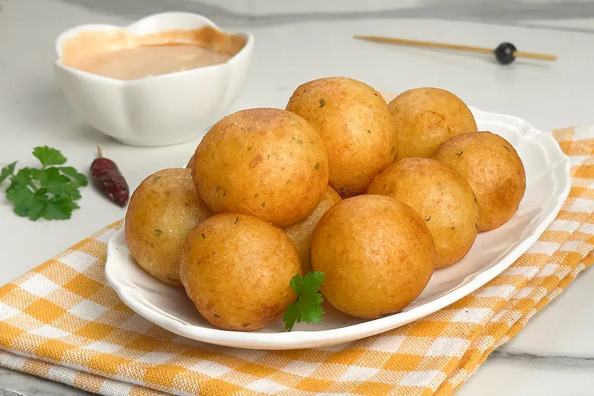 Sfere dorate di patate, un'interpretazione golosa dei frytki po włosku, servite con salsa e guarnite con prezzemolo e peperoncino.