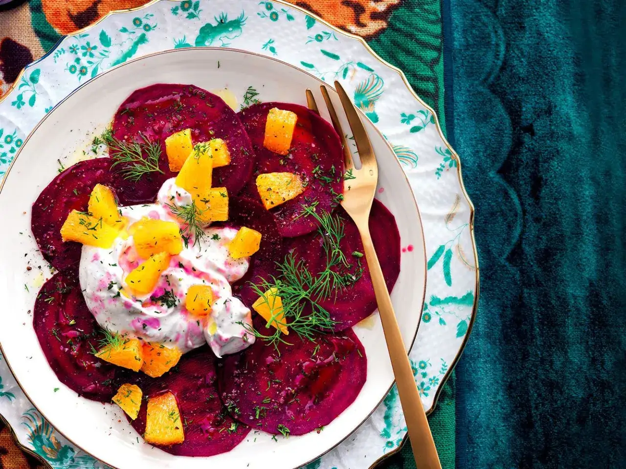 Delizioso carpaccio di barbabietola con crema, arancia e aneto su un piatto decorato.