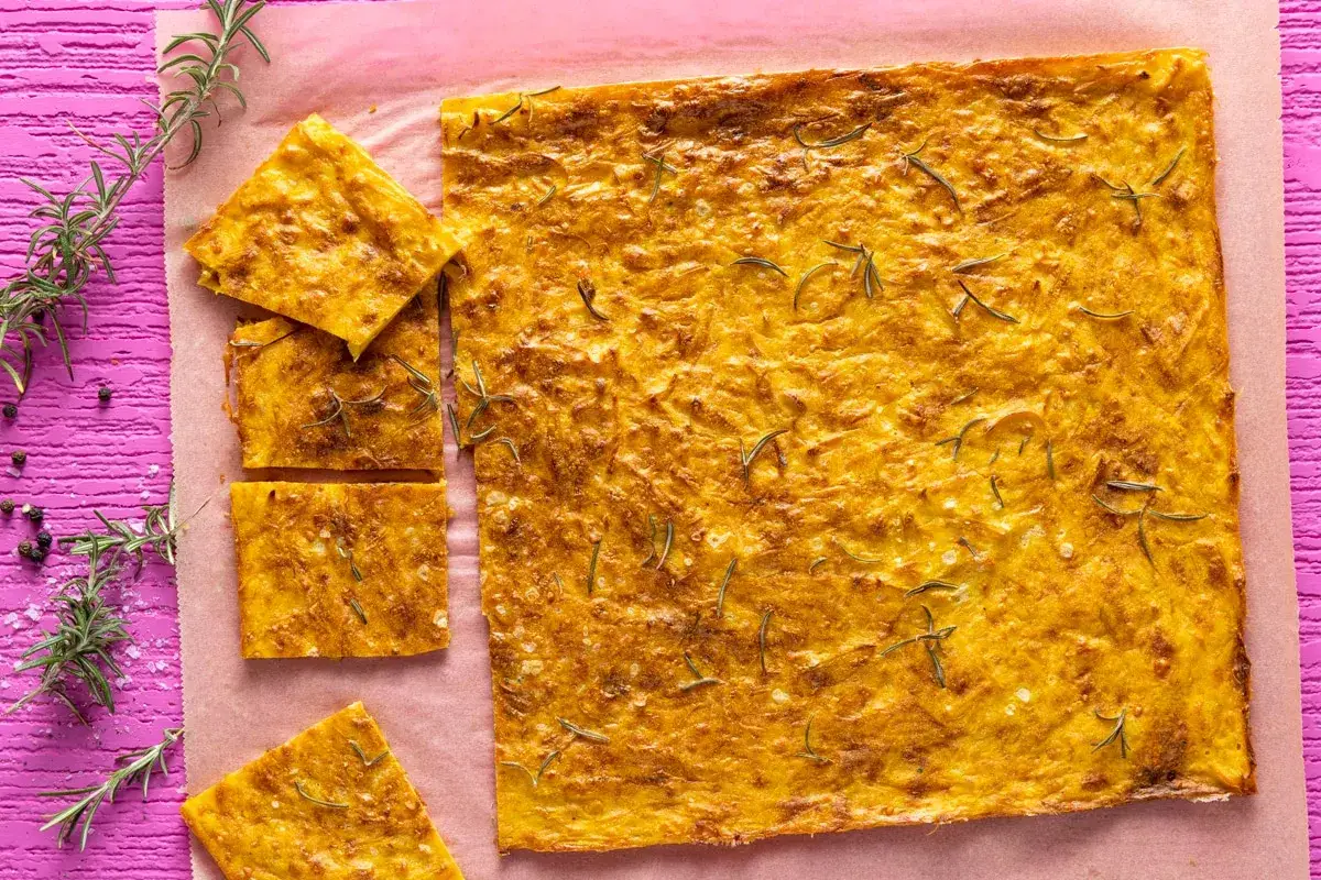 Schiacciata di zucca senza farina, dorata e profumata al rosmarino, tagliata a fette su carta forno.