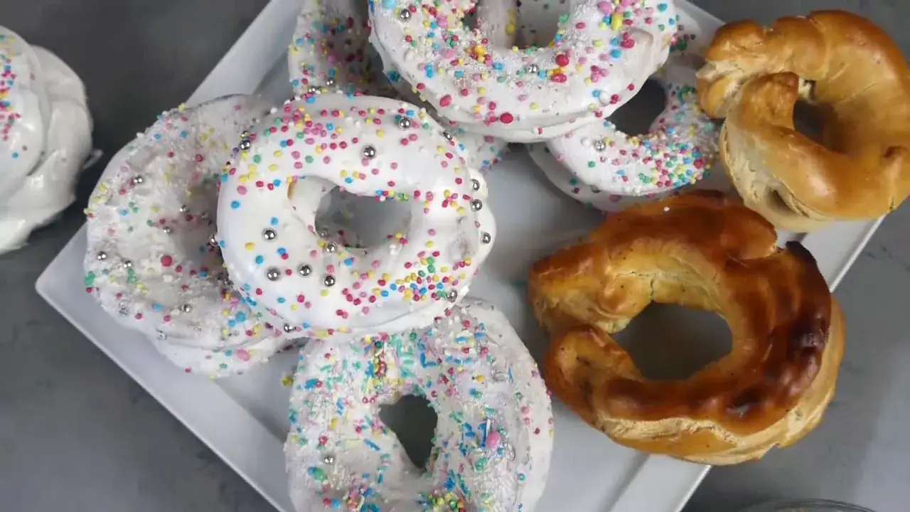 Ciambelle decorate con glassa bianca e zuccherini colorati, accanto a ciambelle dorate e intrecciate. Un delizioso lukier przepis.