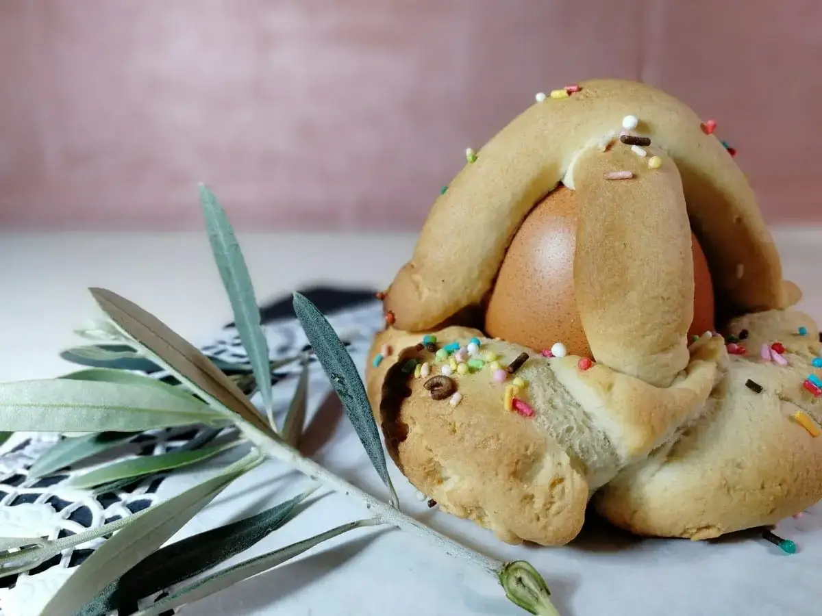 Dolci biscotti pasquali con uovo sodo al centro, decorati con codette colorate e un rametto d'ulivo.