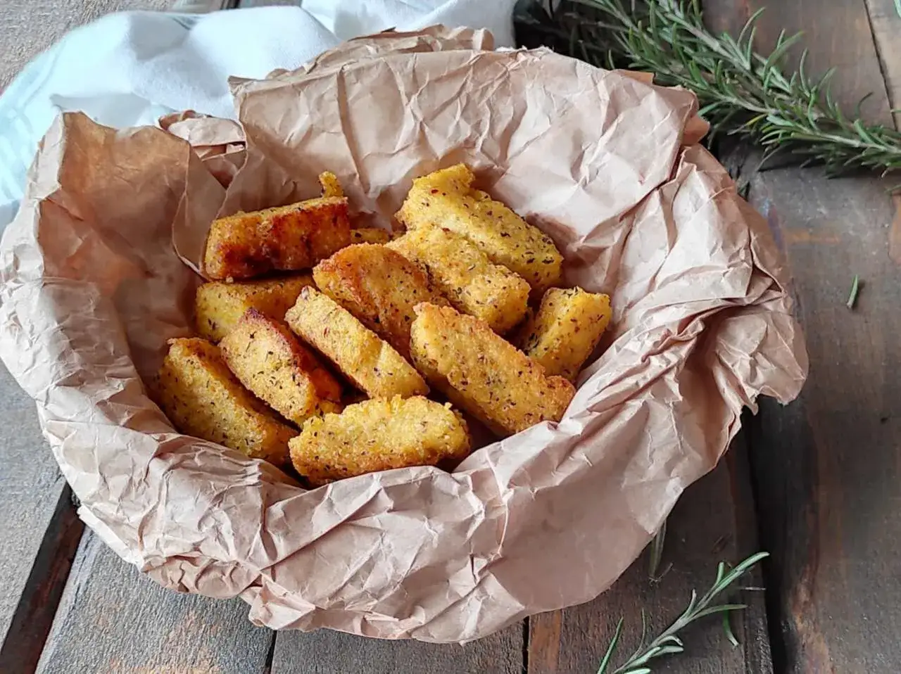 Bastoncini dorati di polenta taragna fritta, croccanti fuori e morbidi dentro, serviti in un cestino di carta da forno.