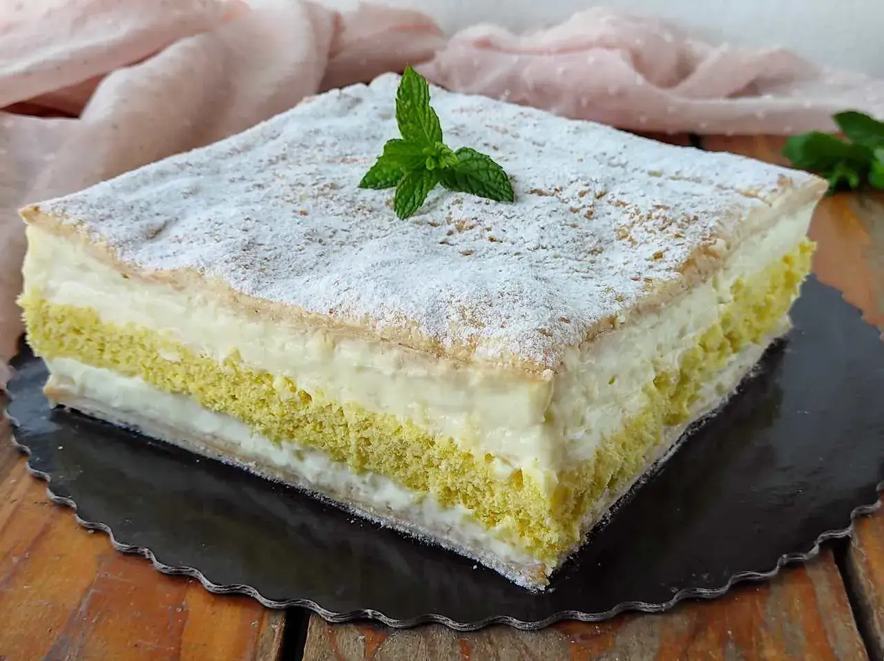 Deliziosa torta di compleanno con pasta sfoglia e pan di spagna, farcita con crema e guarnita con zucchero a velo e menta.
