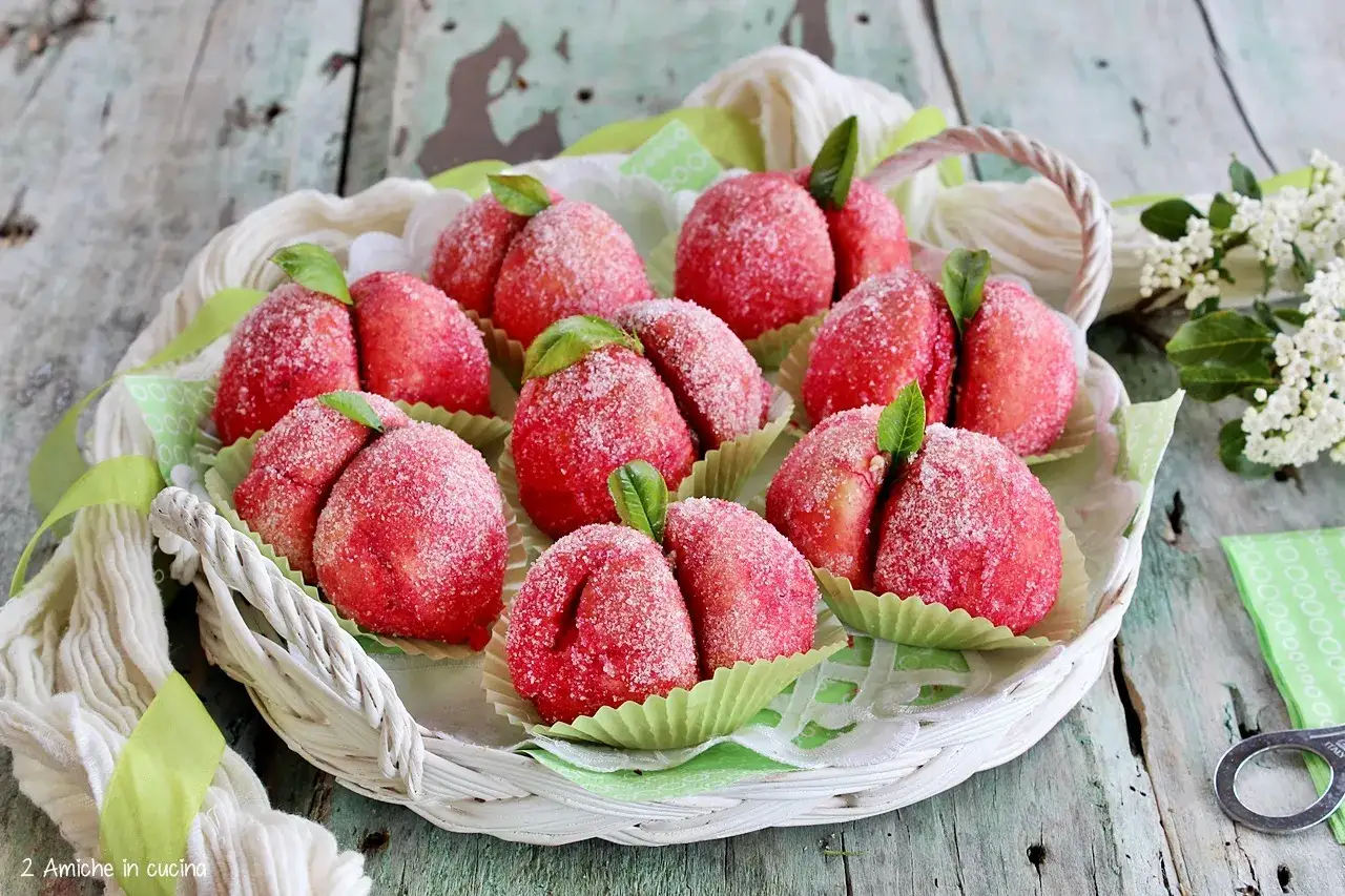 Dolci pesche al cioccolato, ricoperte di zucchero e decorate con foglioline verdi, disposte in un cestino bianco.