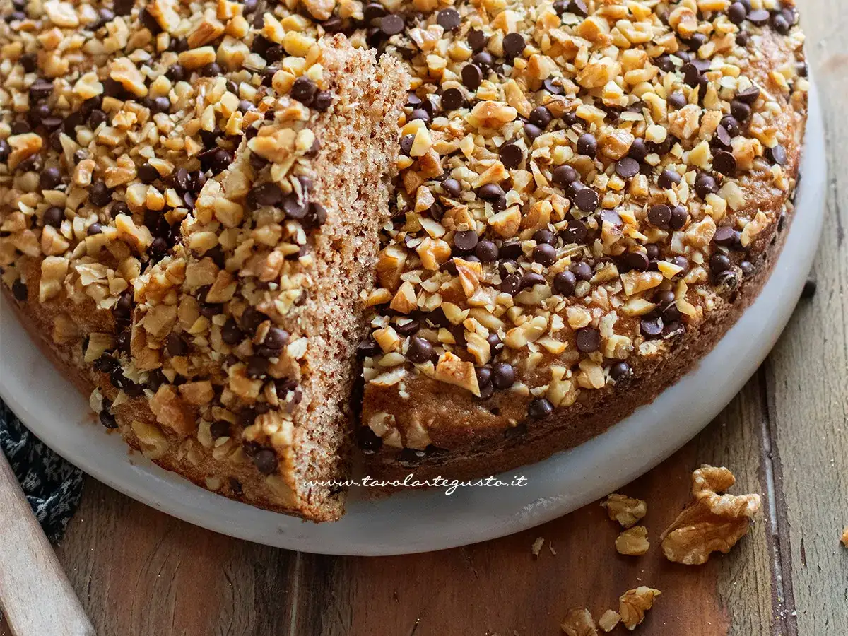 Una fetta di torta di noci della nonna, ricca di noci tritate e gocce di cioccolato, su un piatto bianco.
