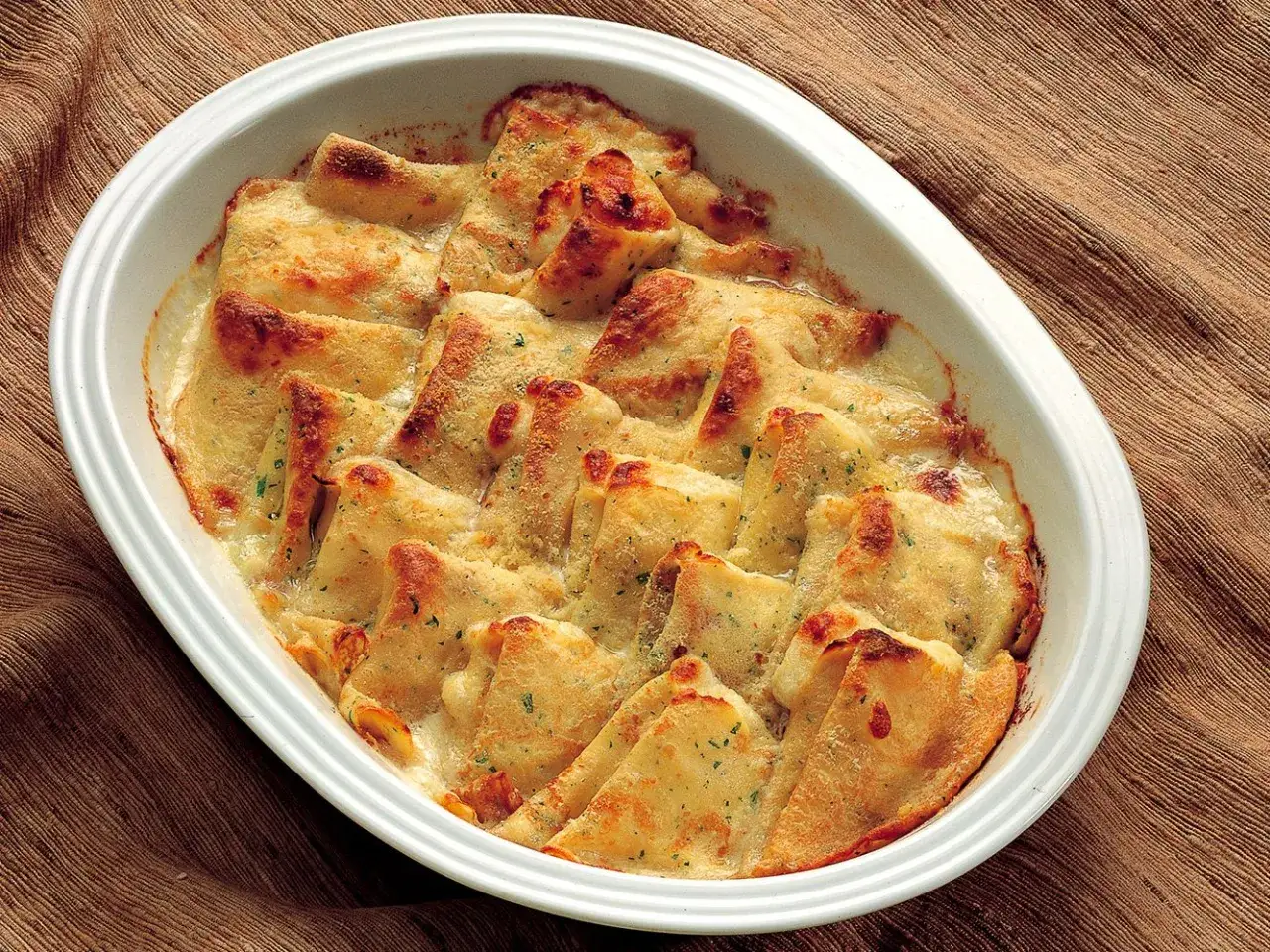 Crepes ai 4 formaggi gratinate in una pirofila bianca, dorate e filanti, pronte per essere gustate.