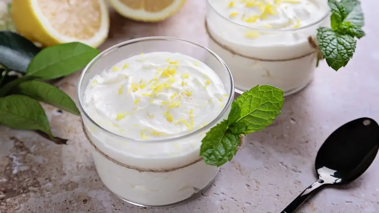 Deliziosa crema al lime in bicchieri di vetro, guarnita con scorza di limone e menta fresca. Accanto, limoni tagliati e un cucchiaio nero.