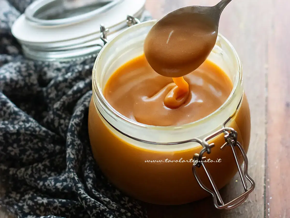 Un cucchiaio solleva la vellutata crema pasticcera al caramello salato da un barattolo di vetro.