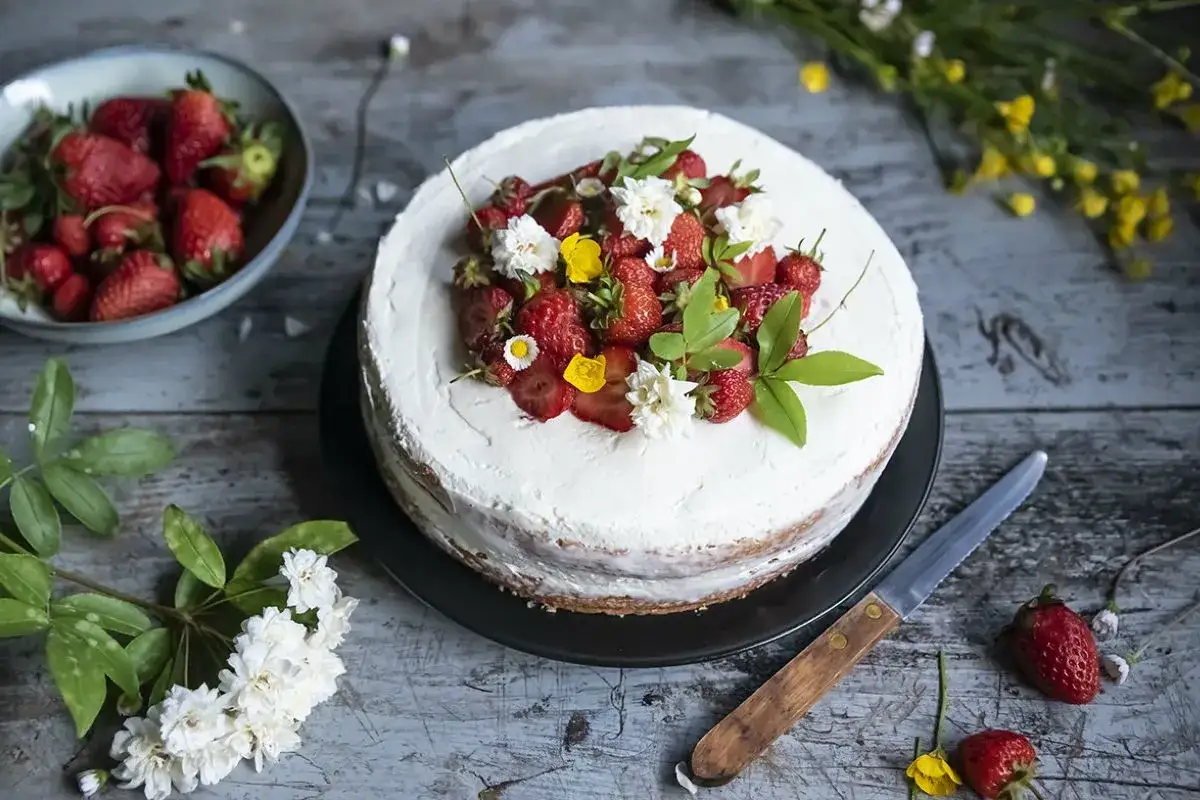 Torta con crema allo yogurt per pan di spagna, decorata con fragole fresche e fiori.