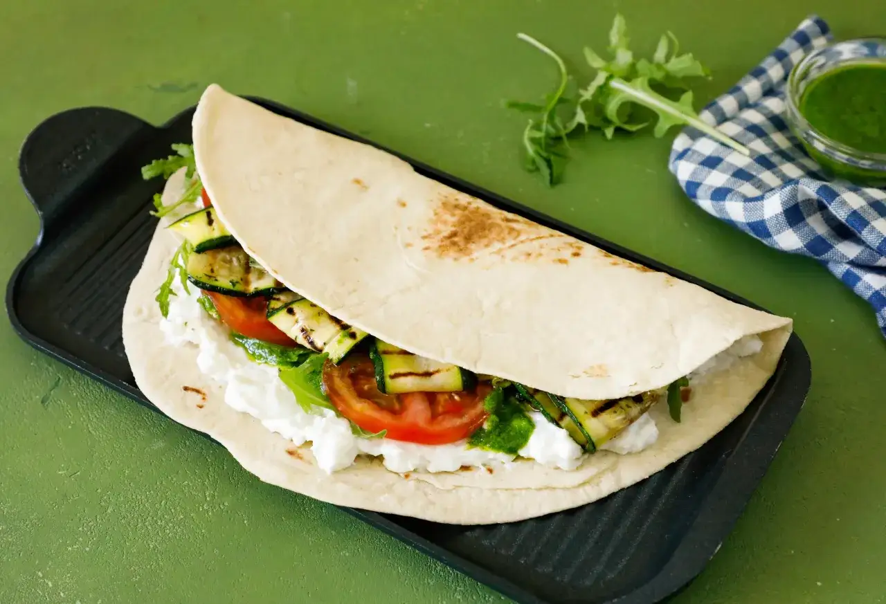 Piadina ripiena di ricotta, pomodoro, zucchine grigliate e un tocco di pesto fresco.