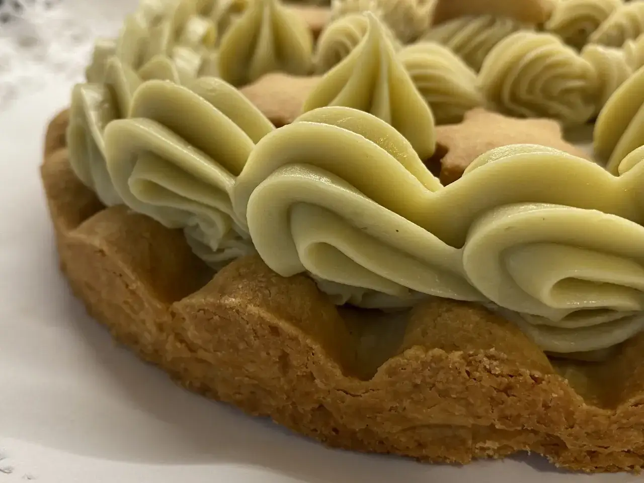 Torta con bordo croccante e decorazioni a ciuffi di ganache pistacchio, intervallate da biscotti a forma di stella.