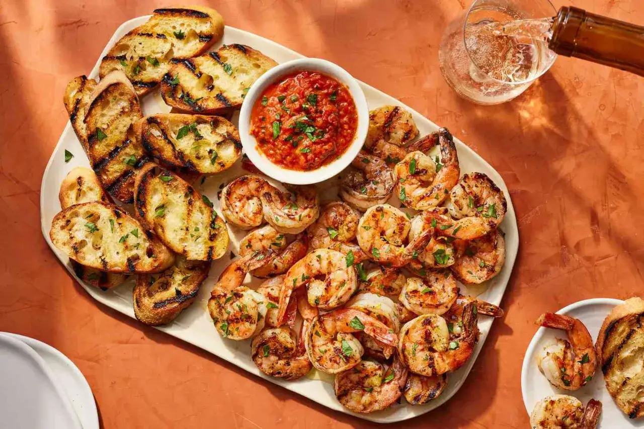 Grigliata di gamberi aperitivo con crostini e salsa rossa. Un bicchiere di vino bianco viene versato.