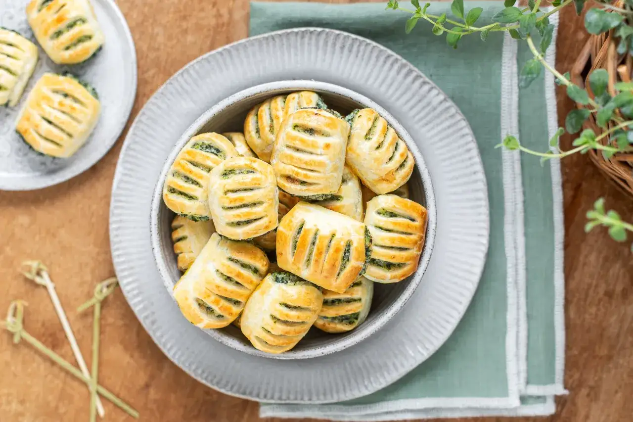Piccoli fagottini dorati con ripieno pasta sfoglia e spinaci, serviti in una ciotola grigia.