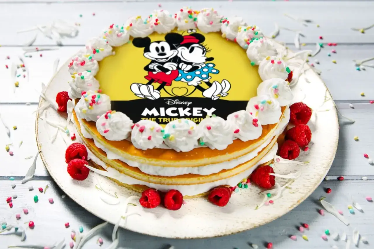 Torta a strati con decorazione di Mickey Mouse, panna montata, lamponi e zuccherini colorati.